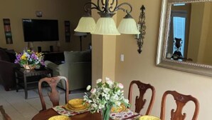 Une salle à manger avec une table en bois dressée pour six personnes, des chaises, un vase rempli de fleurs et un ventilateur de plafond.