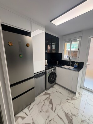 A compact kitchen with a built-in washing machine, a refrigerator, and a window with a view of the outside.