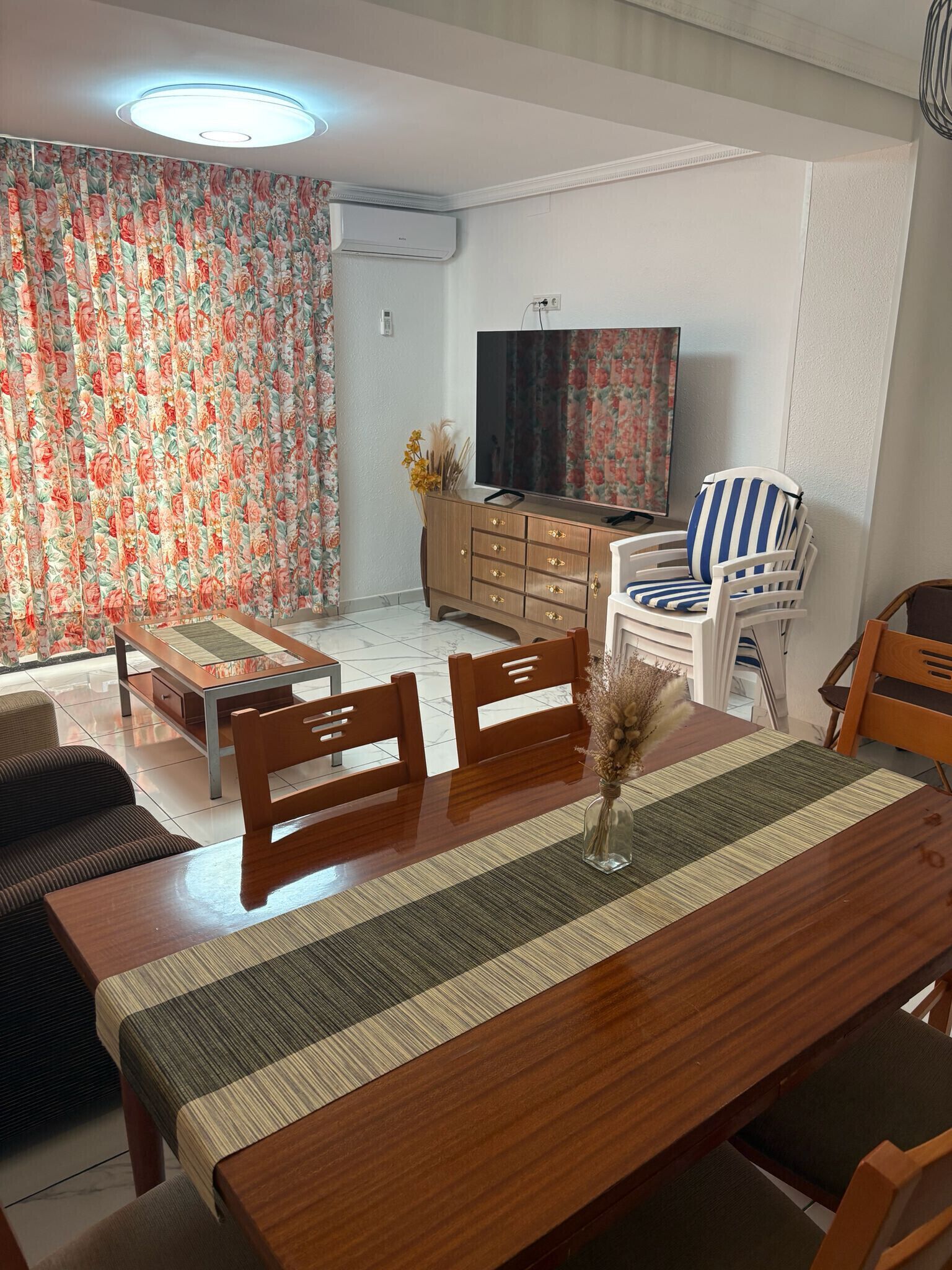 Un salon comprenant une table à manger, des chaises, un canapé, un téléviseur et un rideau à motifs floraux.