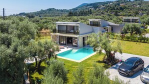 Una villa moderna con piscina, rodeada de exuberante vegetación y montañas al fondo.