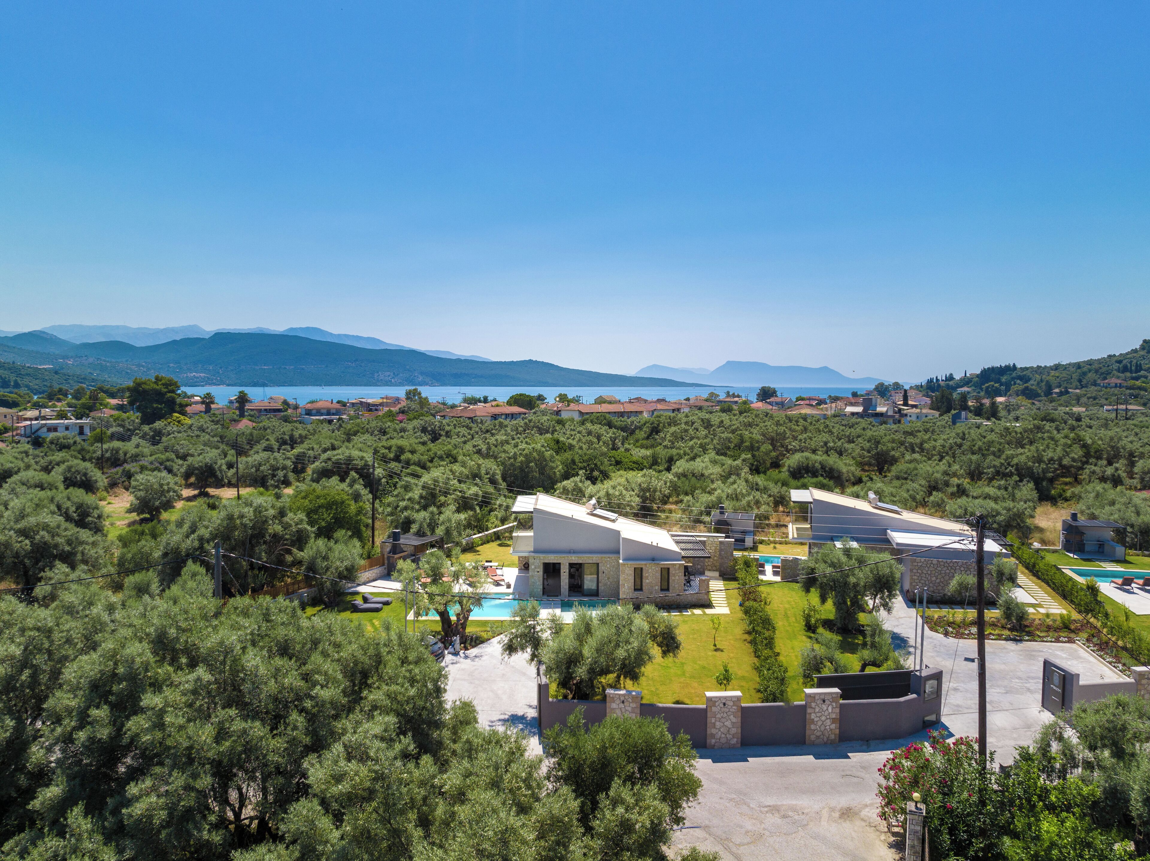 A residential area with a large house featuring a swimming pool, surrounded by lush greenery and a view of the sea and mountains.