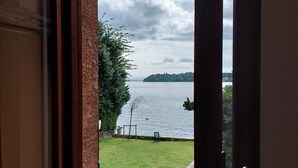 A window with a view of a grassy area, a body of water, and a distant landmass. - Holiday House Camillina (Salò)