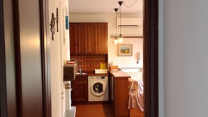 A narrow hallway leading to a kitchen with wooden cabinets, a washing machine, and a tiled backsplash. - Holiday House Camillina (Salò)