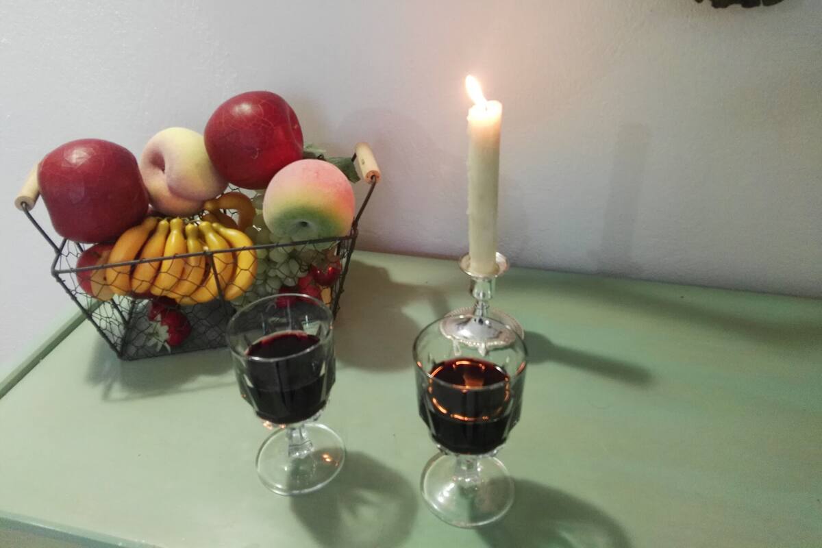 A table with a fruit basket, two wine glasses, and a lit candle.