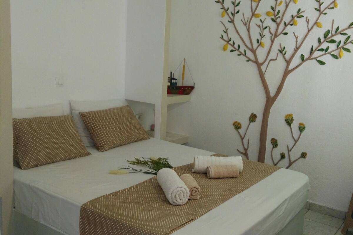 A neatly made bed with a brown polka dot bedspread, two pillows, and rolled towels.