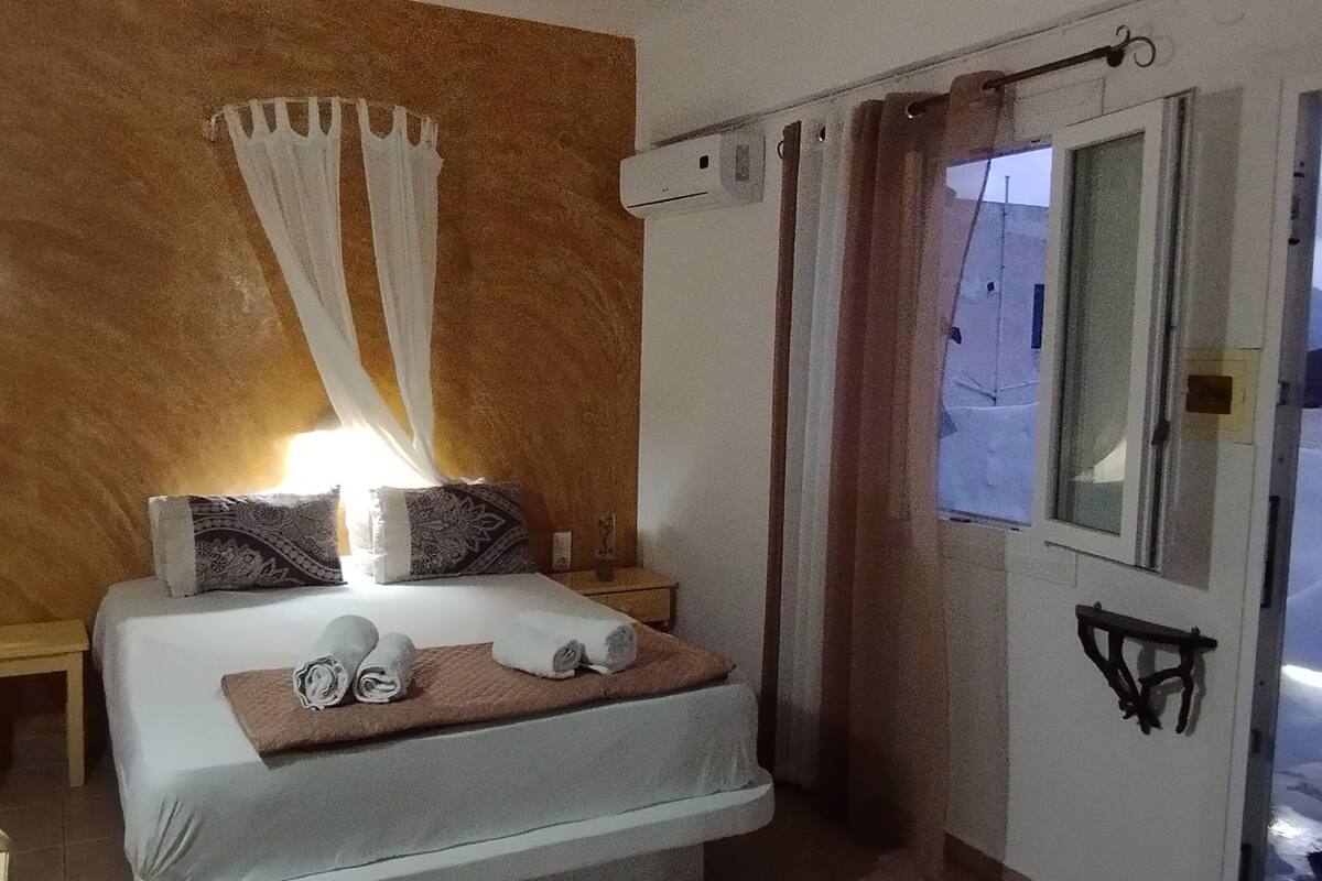 A bedroom with a bed, a bedside table, a window, and a curtain.