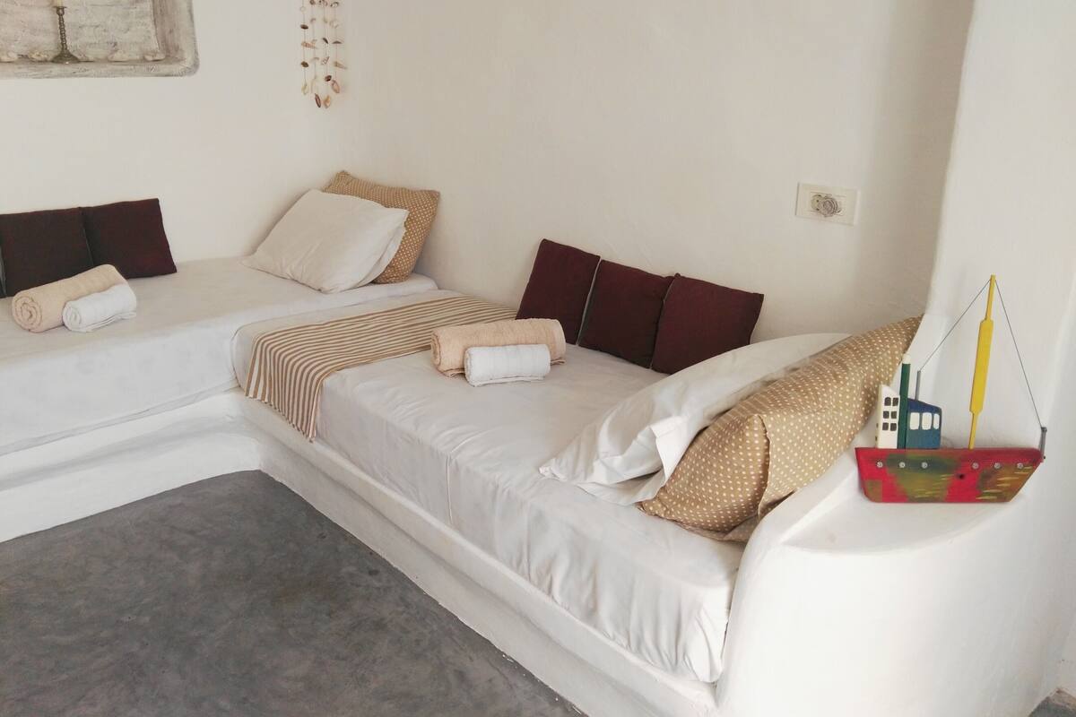 A hotel room with two beds, a dreamcatcher, and a small ship decoration.