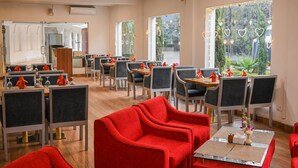 Un comedor con sillas tapizadas en rojo, mesas con servilletas blancas y vistas a la vegetación a través de amplias ventanas.