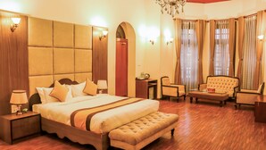 Amplia habitación de hotel con una cama grande, un área de descanso con sofá y sillones, un escritorio pequeño y un candelabro.