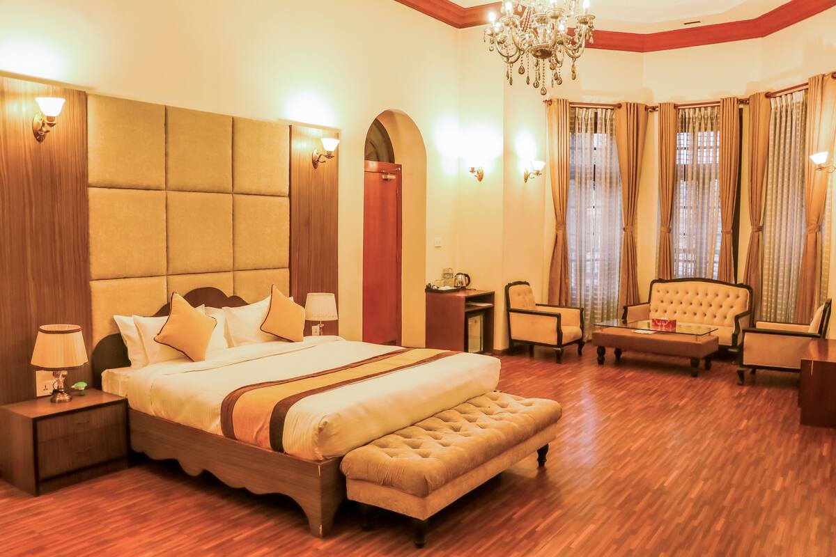 Amplia habitación de hotel con una cama grande, un área de descanso con sofá y sillones, un escritorio pequeño y un candelabro.