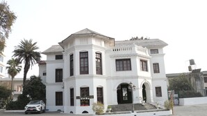 Un edificio blanco con una entrada central, múltiples ventanas y una escalera que conduce a la entrada.