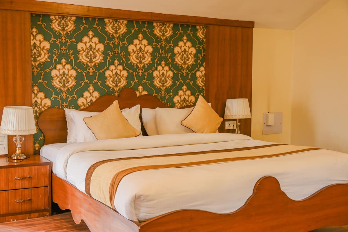 Una cama bien tendida con cabecera de madera, papel tapiz estampado en verde y dos lámparas de noche.