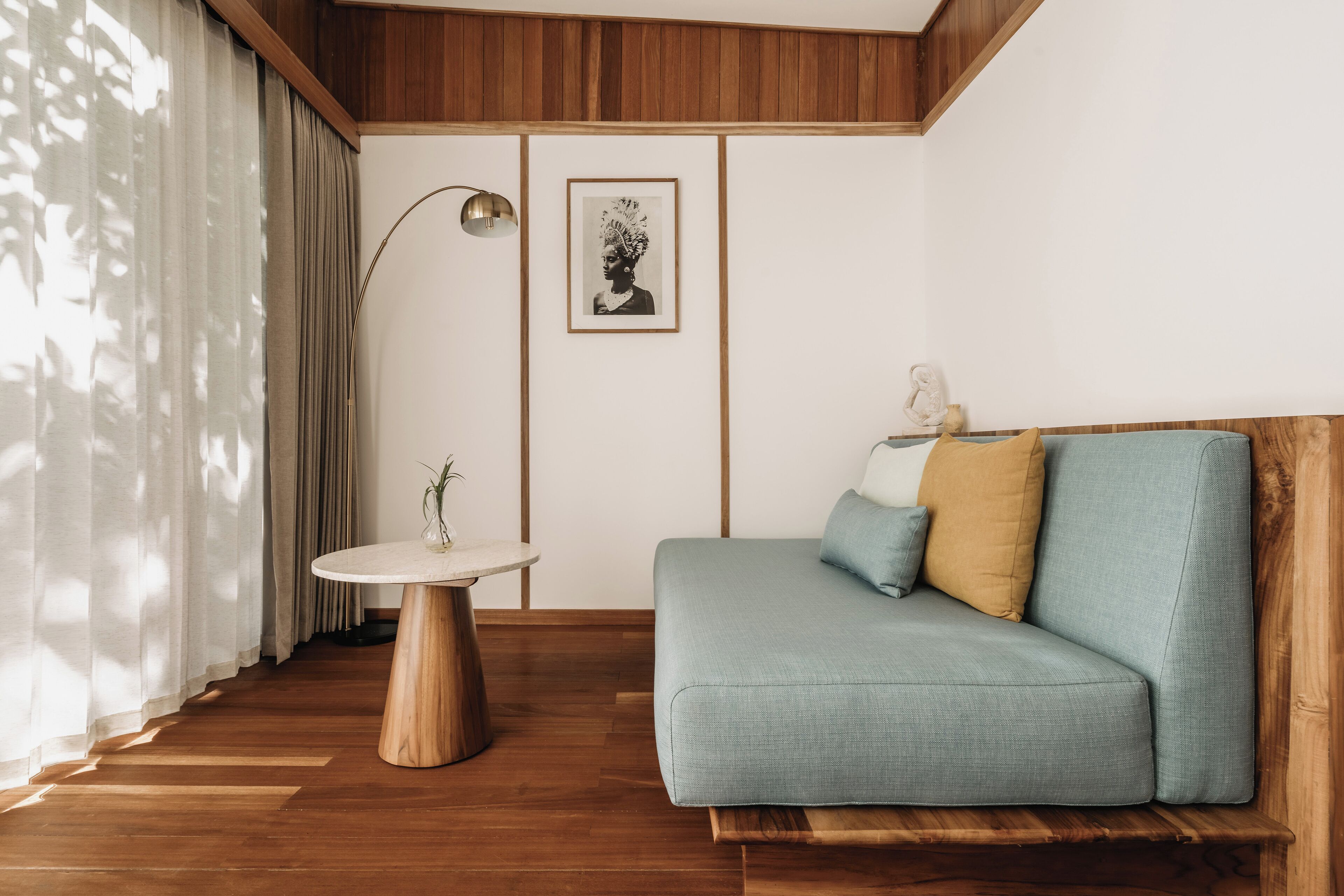 A modern living room with a wooden floor, a blue sofa with cushions, a round wooden table, and a framed picture on the wall.