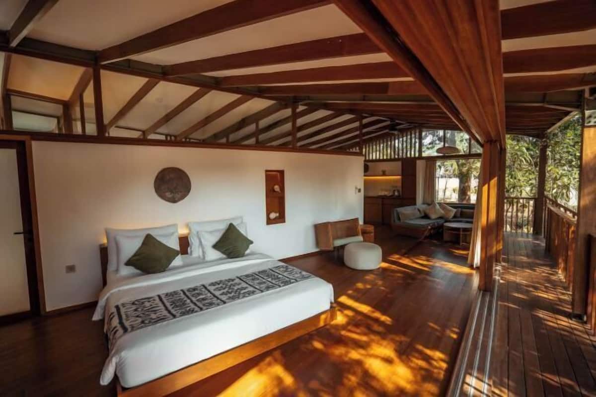 A spacious bedroom with a large bed, a wooden floor, and a view of an outdoor area.