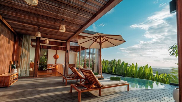 A wooden deck with lounge chairs and a pool, overlooking a lush landscape. - Grün Uluwatu (Pecatu)