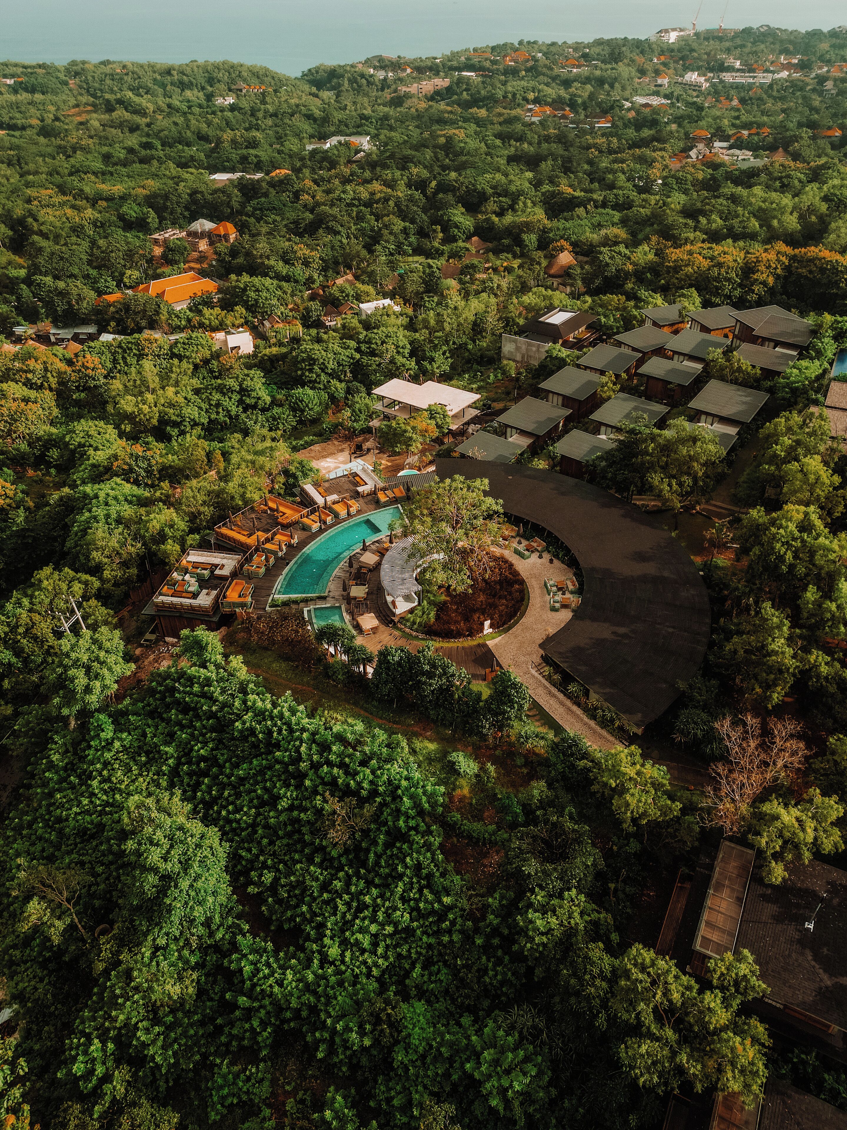 An aerial view of a resort with a swimming pool, guest cabins, and lush greenery.