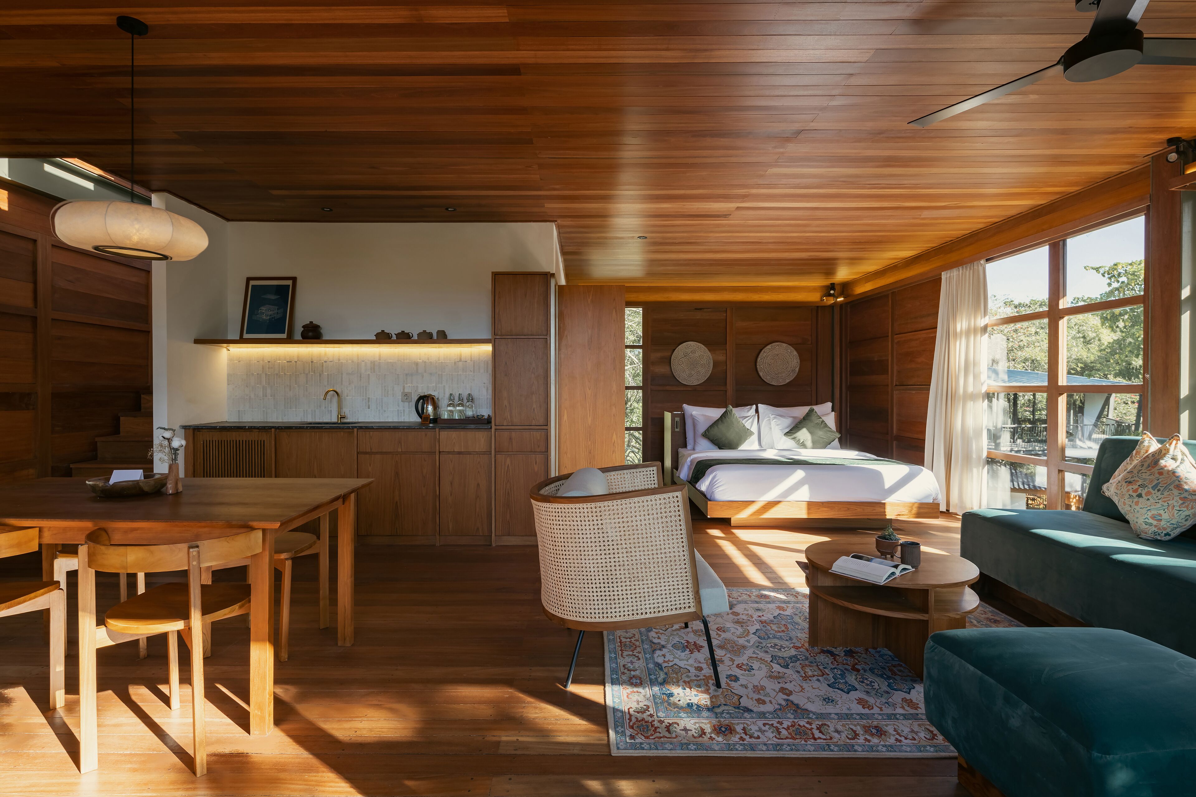 A modern interior with a wooden ceiling, a dining area, a bedroom with a bed and pillows, a sofa, and a small table.