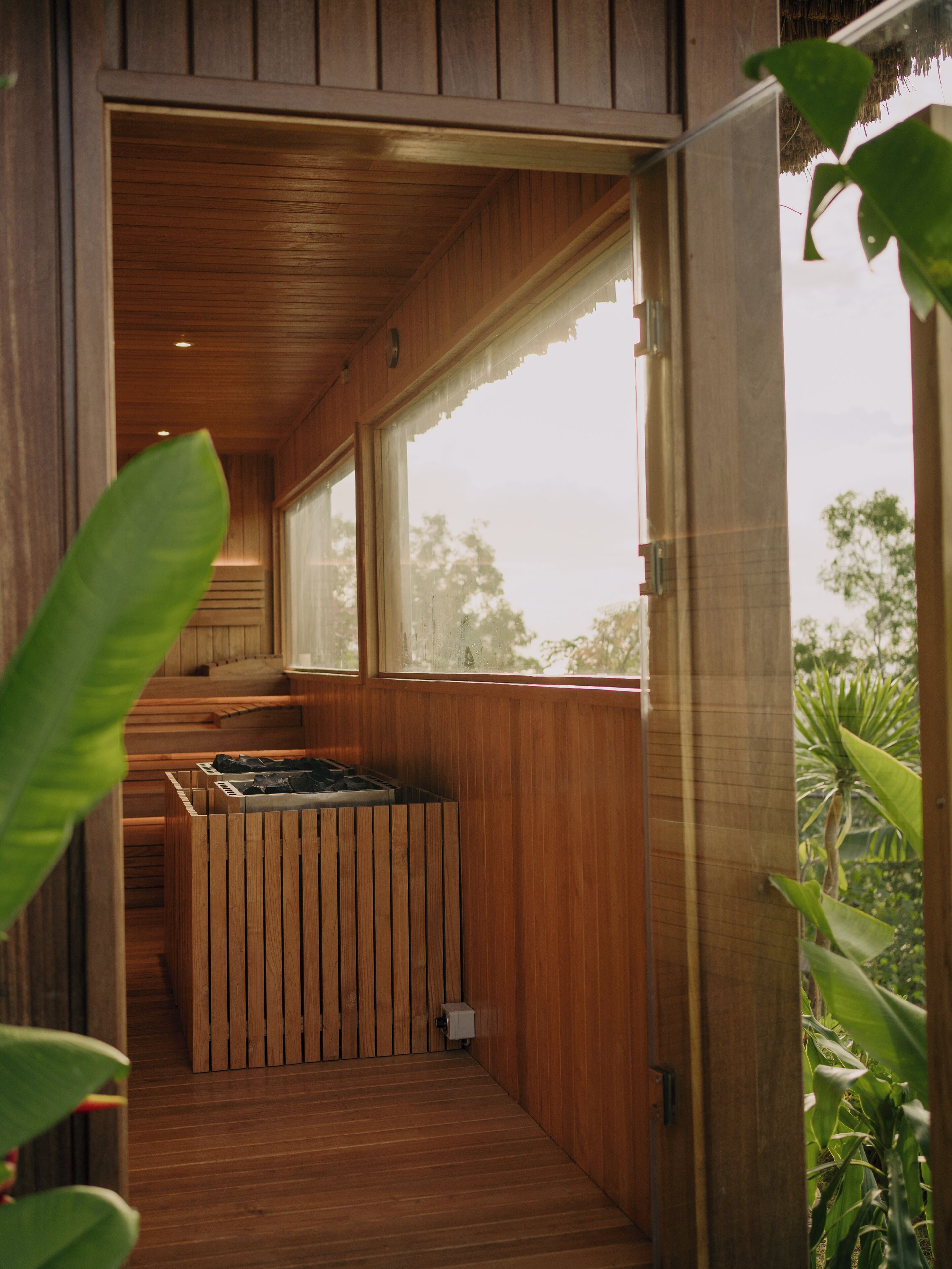 A wooden interior with a built-in stove, large windows, and a view of greenery outside.