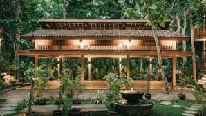 A wooden pavilion with a tiled roof surrounded by lush greenery and potted plants. - Grün Uluwatu (Pecatu)