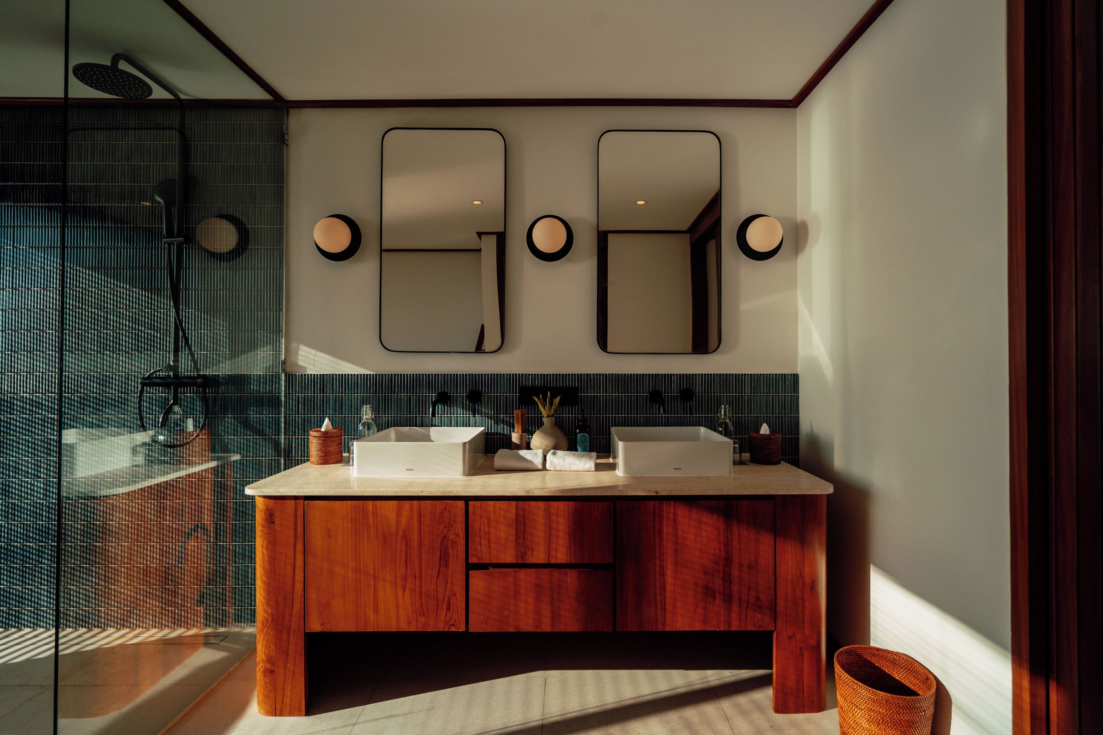 A modern bathroom with a wooden vanity, two mirrors, and a glass shower enclosure.