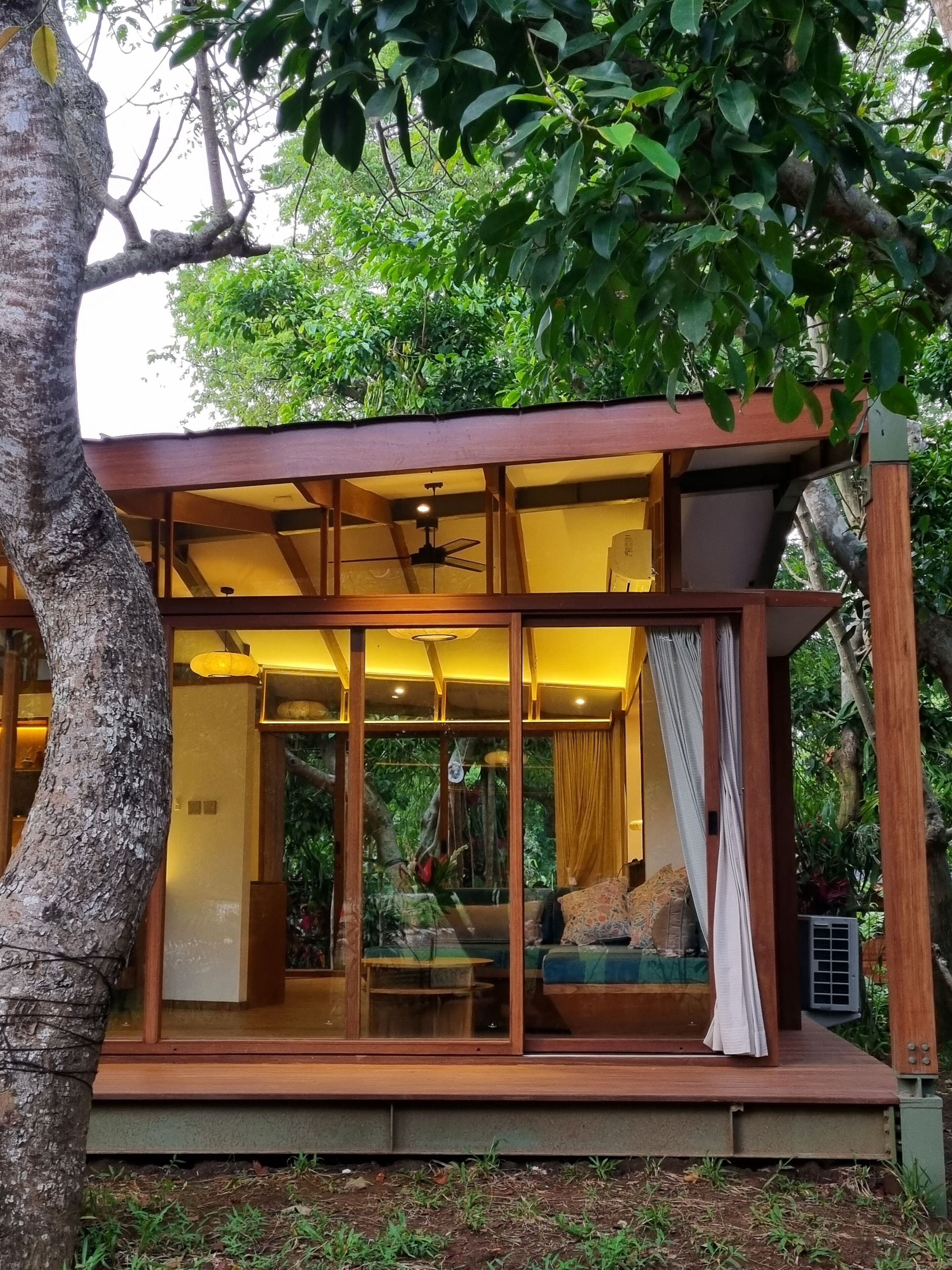 A modern, glass-enclosed cabin with a wooden deck, built-in seating, and a ceiling fan.