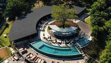 An aerial view of a resort with a central pool, multiple deck areas with seating, and lush surrounding greenery.