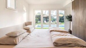 Un dormitorio con una cama grande, una silla y vista a una piscina por una puerta de vidrio.