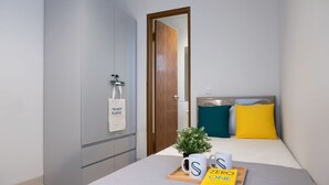 Una habitación de hotel con una cama, una mesita de noche con un libro, una bandeja con una taza y una planta, y un perchero en la pared con una bolsa que dice 'No soy plástico'.