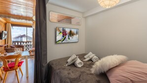 Une chambre d’hôtel comprenant un lit, un téléviseur fixé au mur, une fenêtre donnant sur un immeuble, ainsi qu’un coin repas avec des chaises et une table.