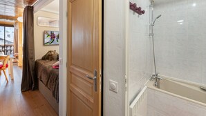 Une chambre d’hôtel avec une porte en bois, un espace douche délimité par une paroi en verre, et une vue sur l’extérieur grâce à une porte ouverte.