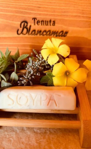 Una caja de madera con una barra de jabón blanca etiquetada como "SOYPA" y flores amarillas.