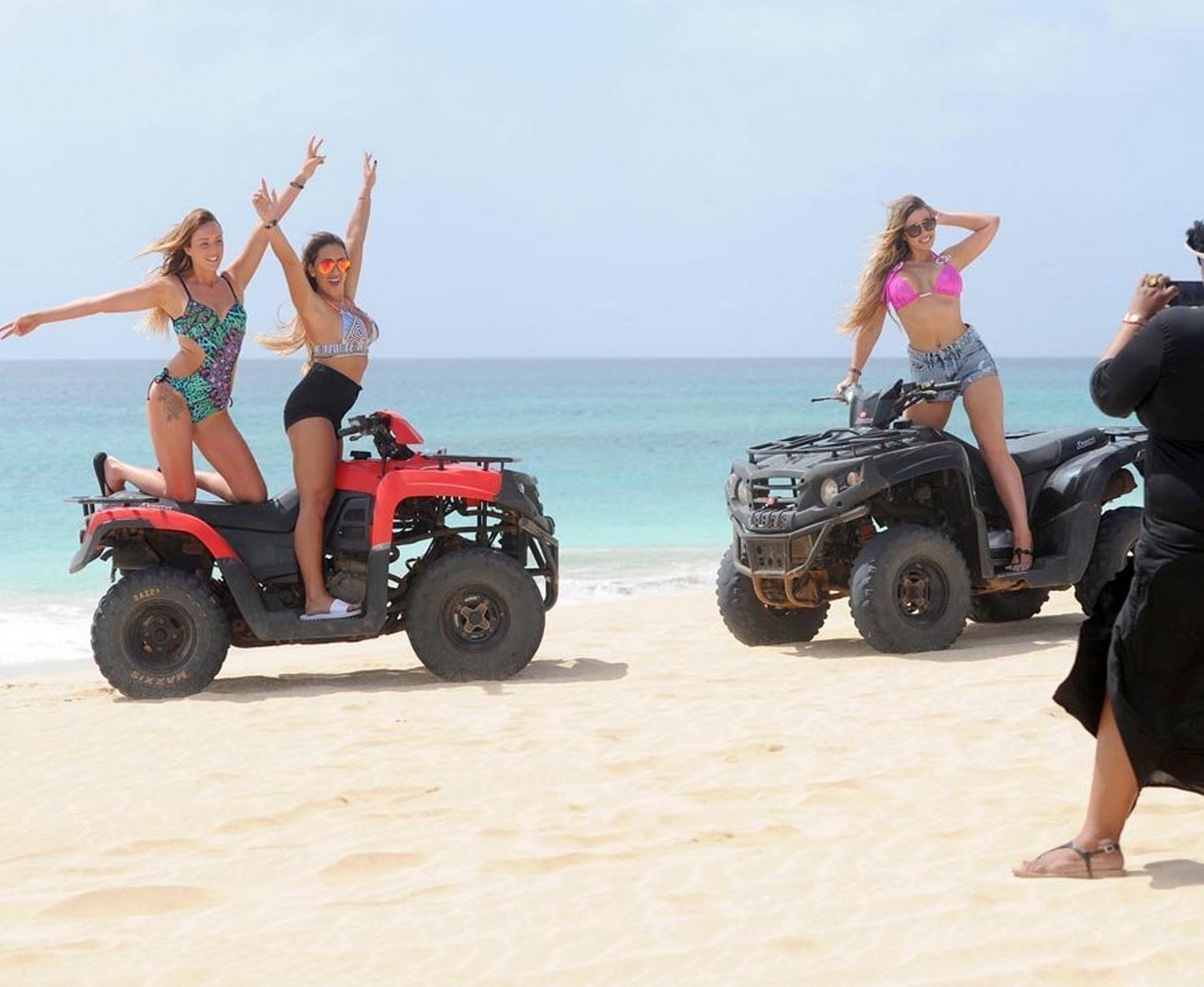 A beach scene with two ATVs and people on them.