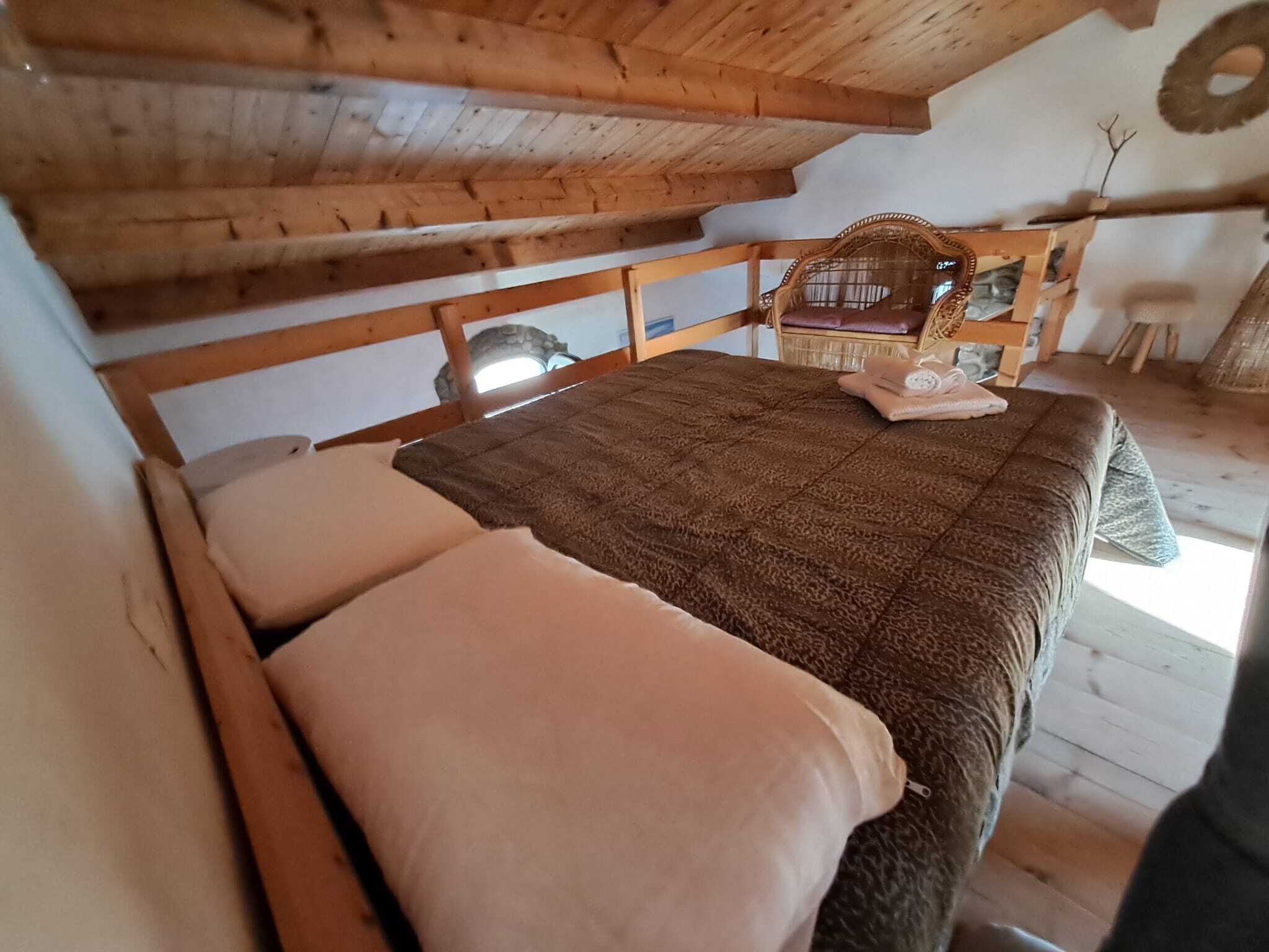Una habitación acogedora con una cama de madera, un sillón tejido y una mesita.