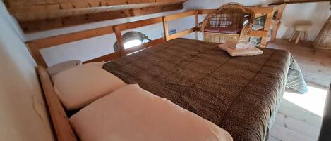 Una habitación acogedora con una cama de madera, un sillón tejido y una mesita.