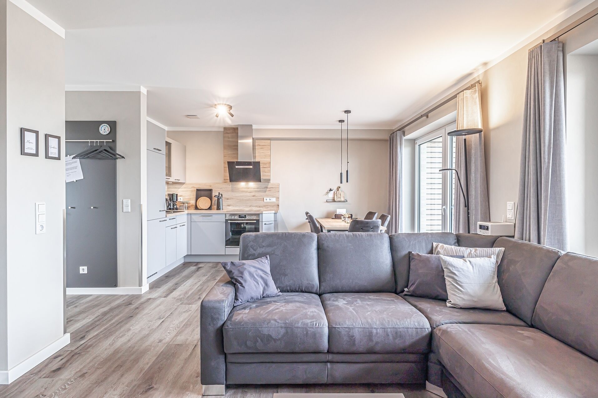 A modern living room with a grey sofa, a dining area, and a kitchen in the background.