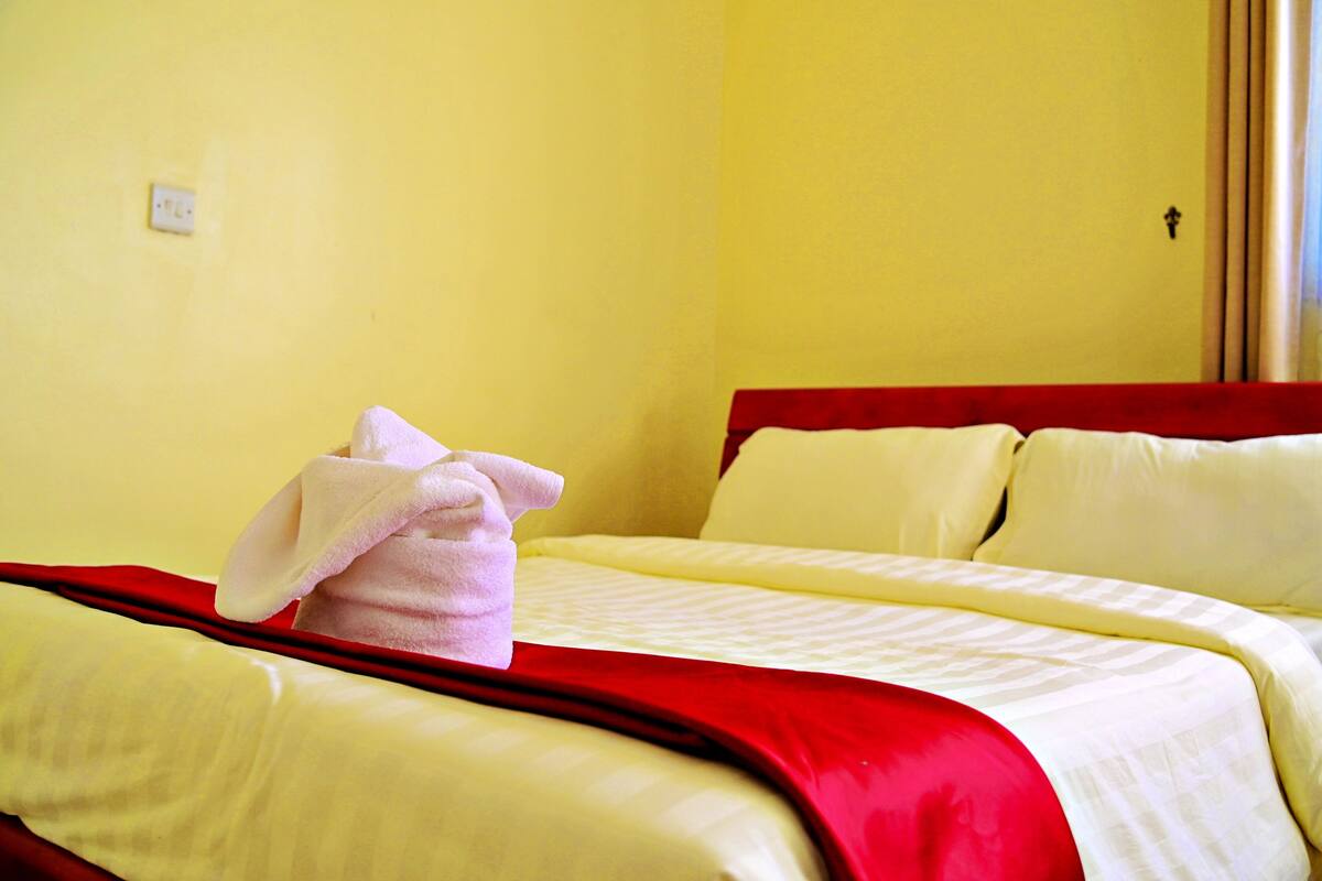 A hotel room with a bed, a red headboard, and a single light switch on the wall.