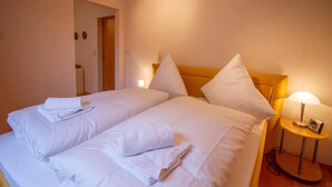 Een hotelkamer met twee bedden, witte lakens, een houten hoofdbord, een nachtkastje met een lamp en een deur naar een andere kamer.