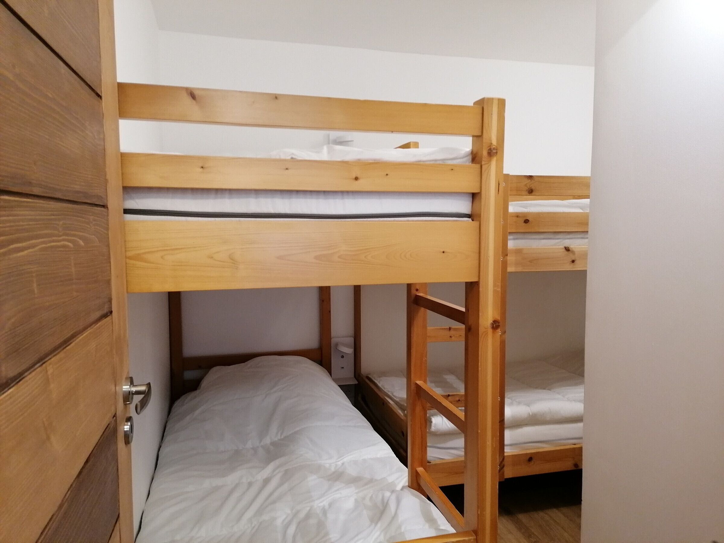 A bunk bed with a wooden frame, white bedding, and a wooden door with a handle.