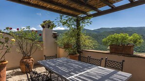 A terrace with a table and chairs, potted plants, and a view of mountains. - 'Torre del Falco', a wonderful medieval tower in Spoleto (Spoleto)