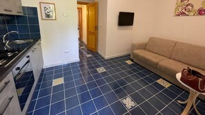 Une cuisine avec des carreaux bleus, un canapé beige et un téléviseur fixé au mur.