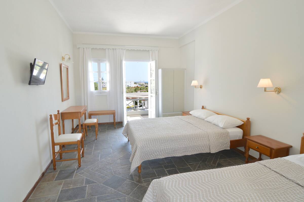 A hotel room with two beds, a desk, chairs, and a TV.