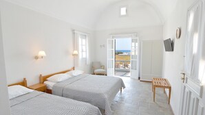 A hotel room with two beds, a wooden bench, a TV mounted on the wall, and a view of the outdoors through an open door. - Nostos Studio (Santorini)