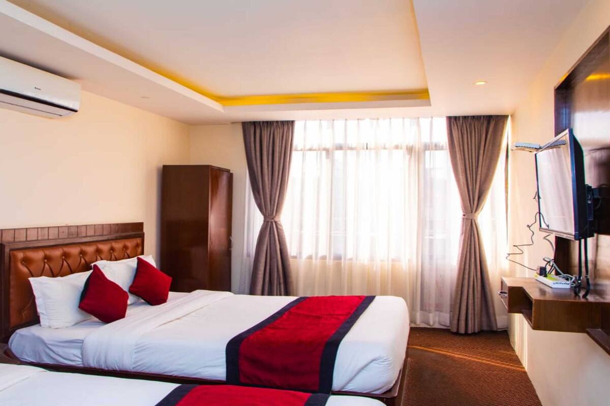 A hotel room with two beds, a television, an air conditioning unit, and a minibar.