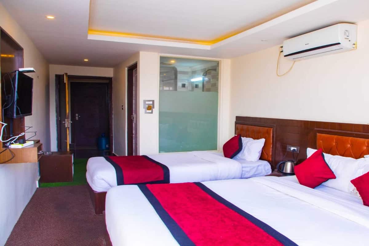 A hotel room with two beds, a television mounted on the wall, and an air conditioning unit.