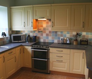 A kitchen with light wooden cabinets, a stainless steel stove, a microwave, and a toaster. - Pet friendly 'Home from Home in the Wye Valley Wales (Chepstow)