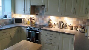 A kitchen with white cabinets, a microwave, a stove, and a kettle. - Pet friendly 'Home from Home in the Wye Valley Wales (Chepstow)