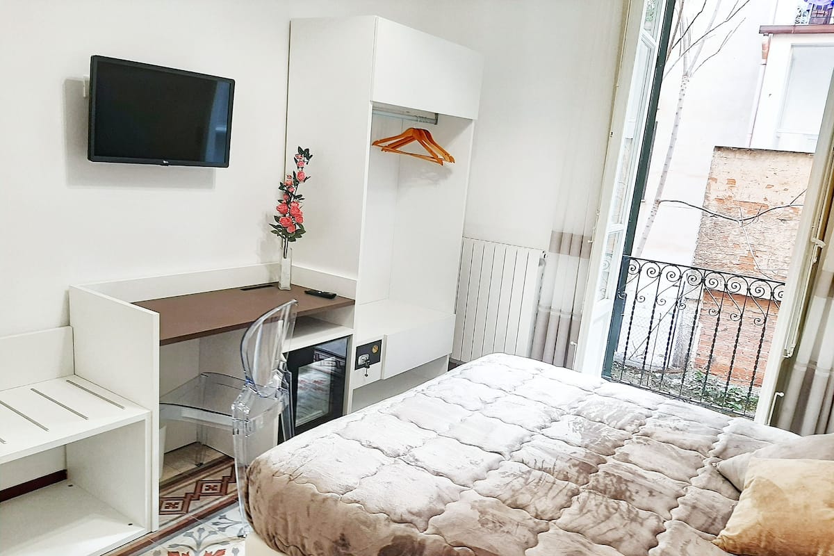Une chambre à coucher comprenant un lit, un bureau, une chaise, un téléviseur et une fenêtre donnant sur l’extérieur.