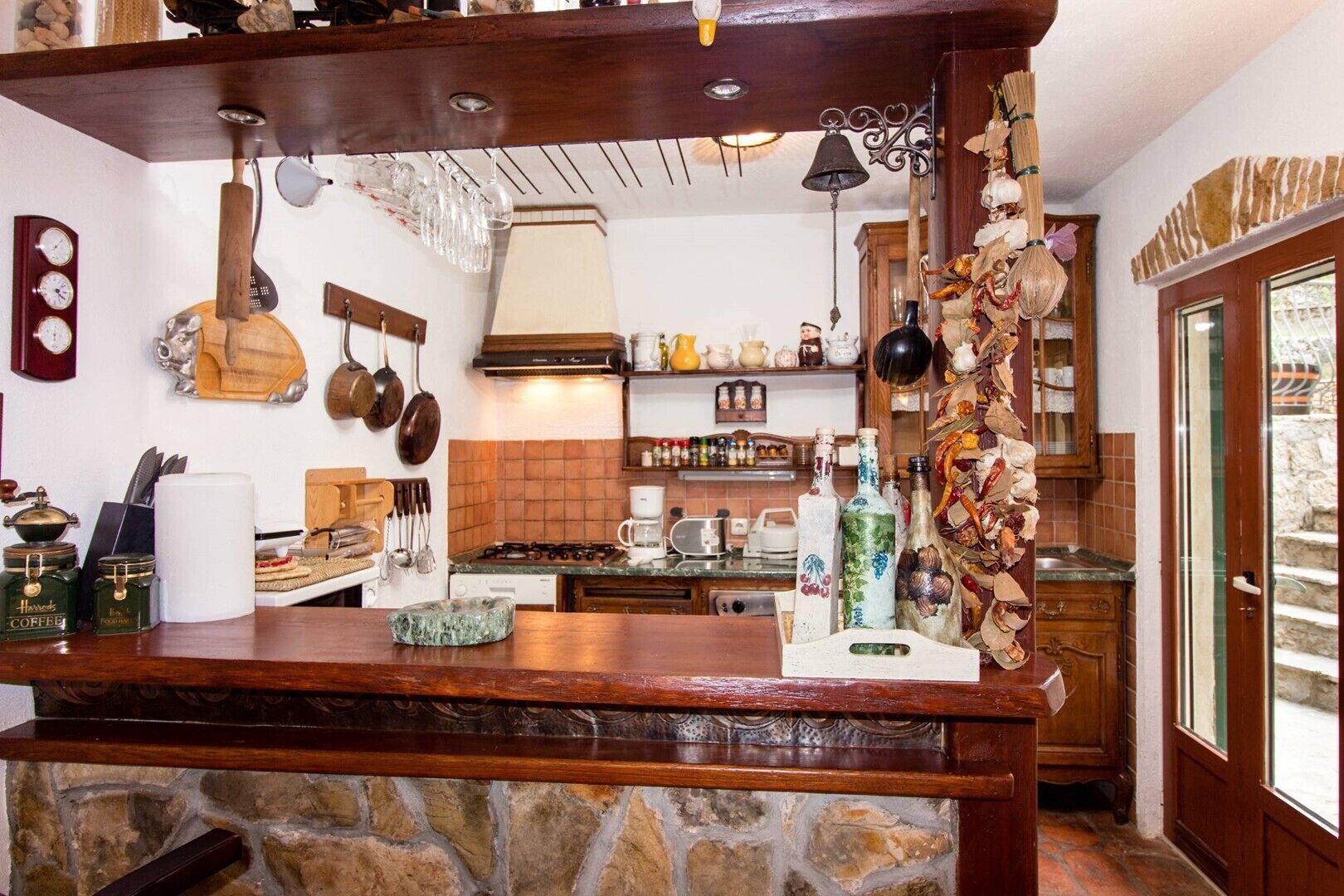 A rustic kitchen with a stone countertop, hanging pots, a wooden bar, and a variety of kitchen utensils and appliances.