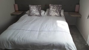 A neatly made bed with a white duvet and two patterned pillows, flanked by two bedside tables with lamps, in a room with plain walls and a simple headboard. - Peaceful "Coorie-in" Boat of Garten (Boat of Garten)