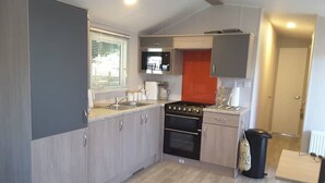 A compact kitchen with grey cabinets, a black stove, and a window with blinds. - Peaceful "Coorie-in" Boat of Garten (Boat of Garten)